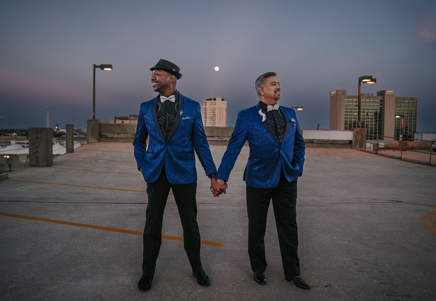 Grooms hold hands as the sun sets on the city of Jacksonville Florida with the skyline behind them