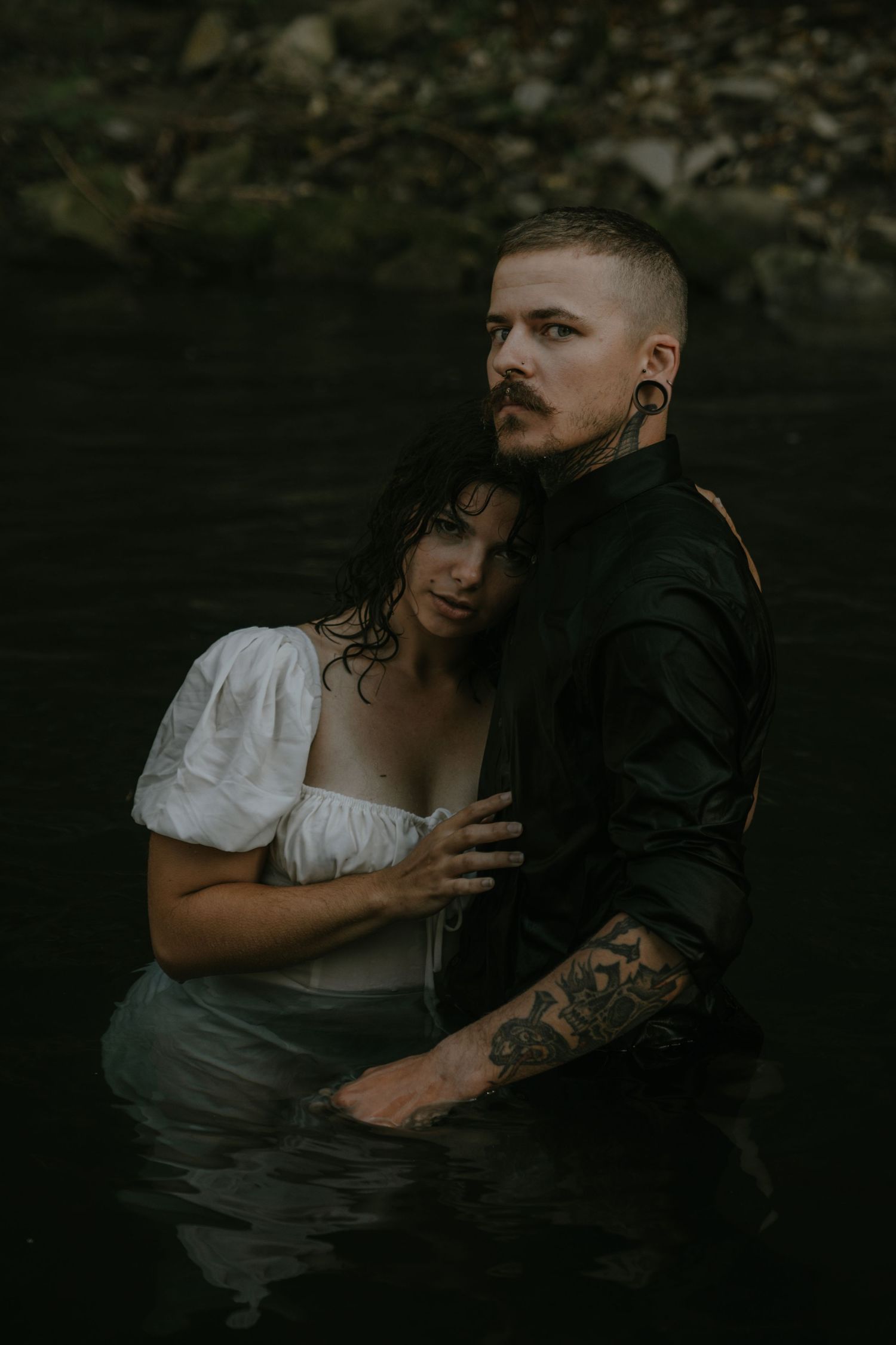 Couple poses in dark water for artistic portrait with dramatic lighting.