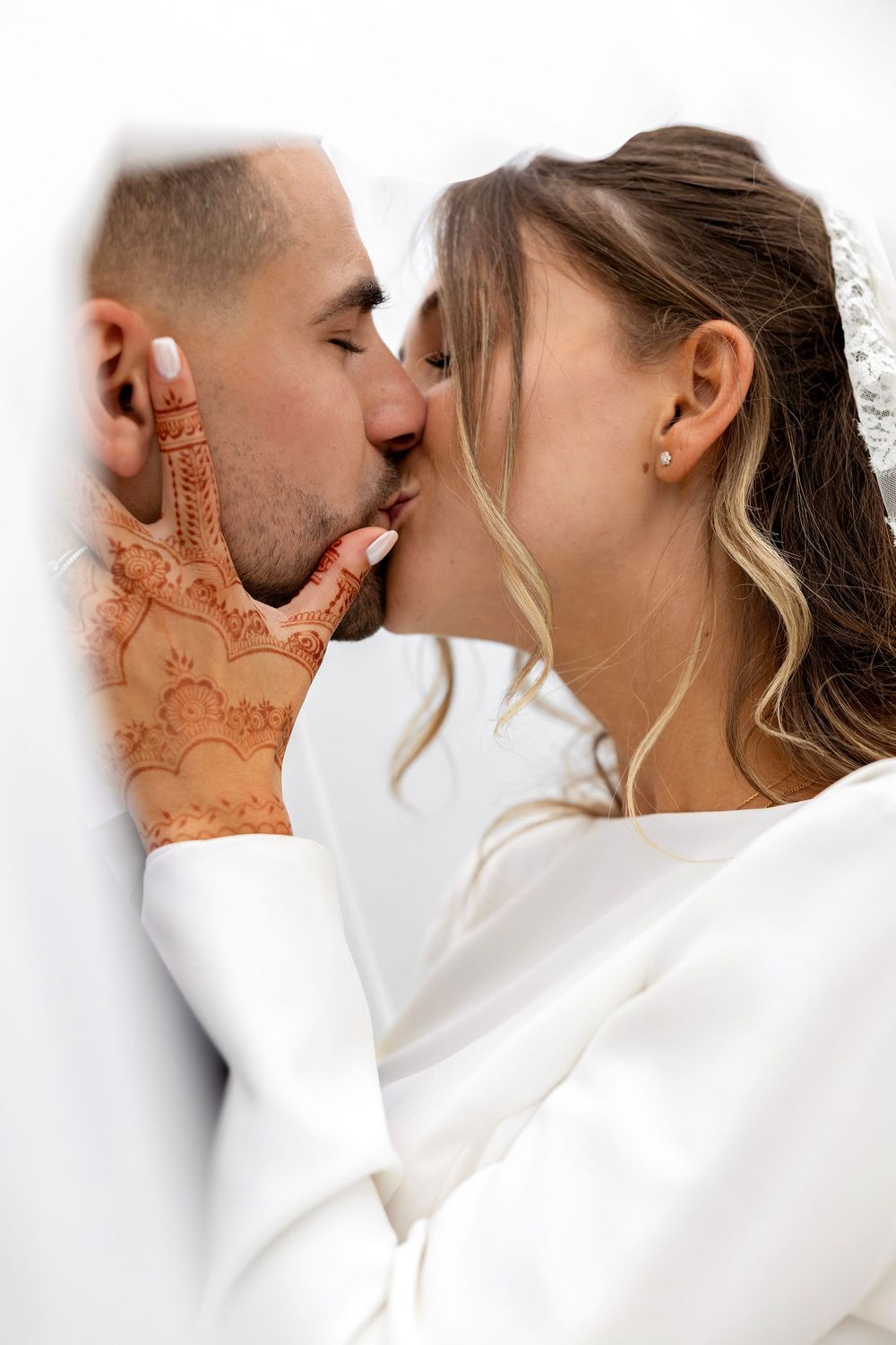 Bride and groom sharing a romantic kiss, bride's hand adorned with traditional henna mehndi design.