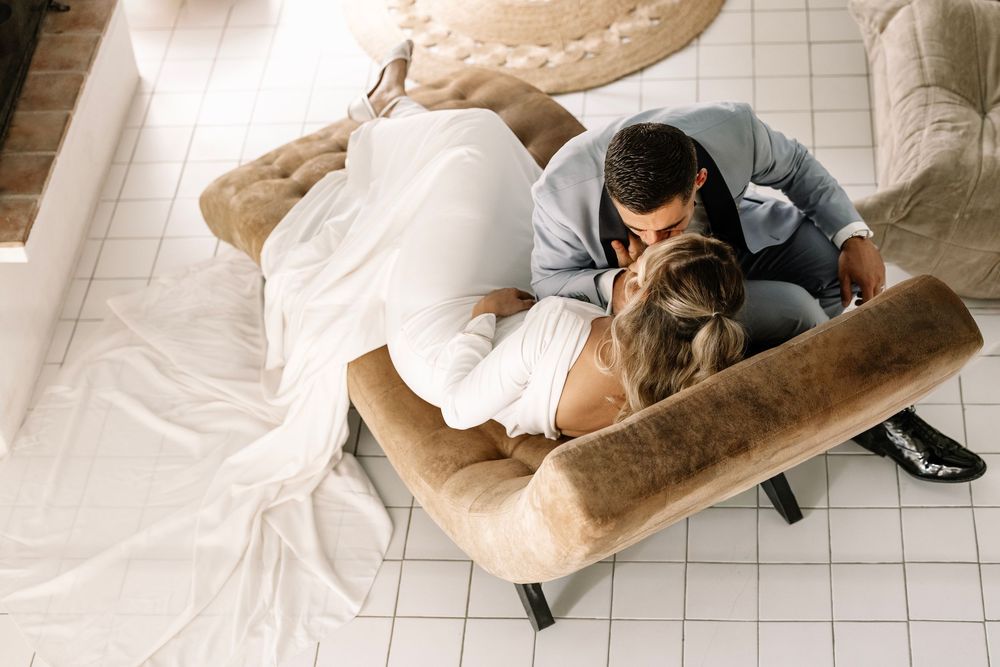 Couple sharing a romantic kiss on a beige sofa, viewed from above in a bright modern living room.