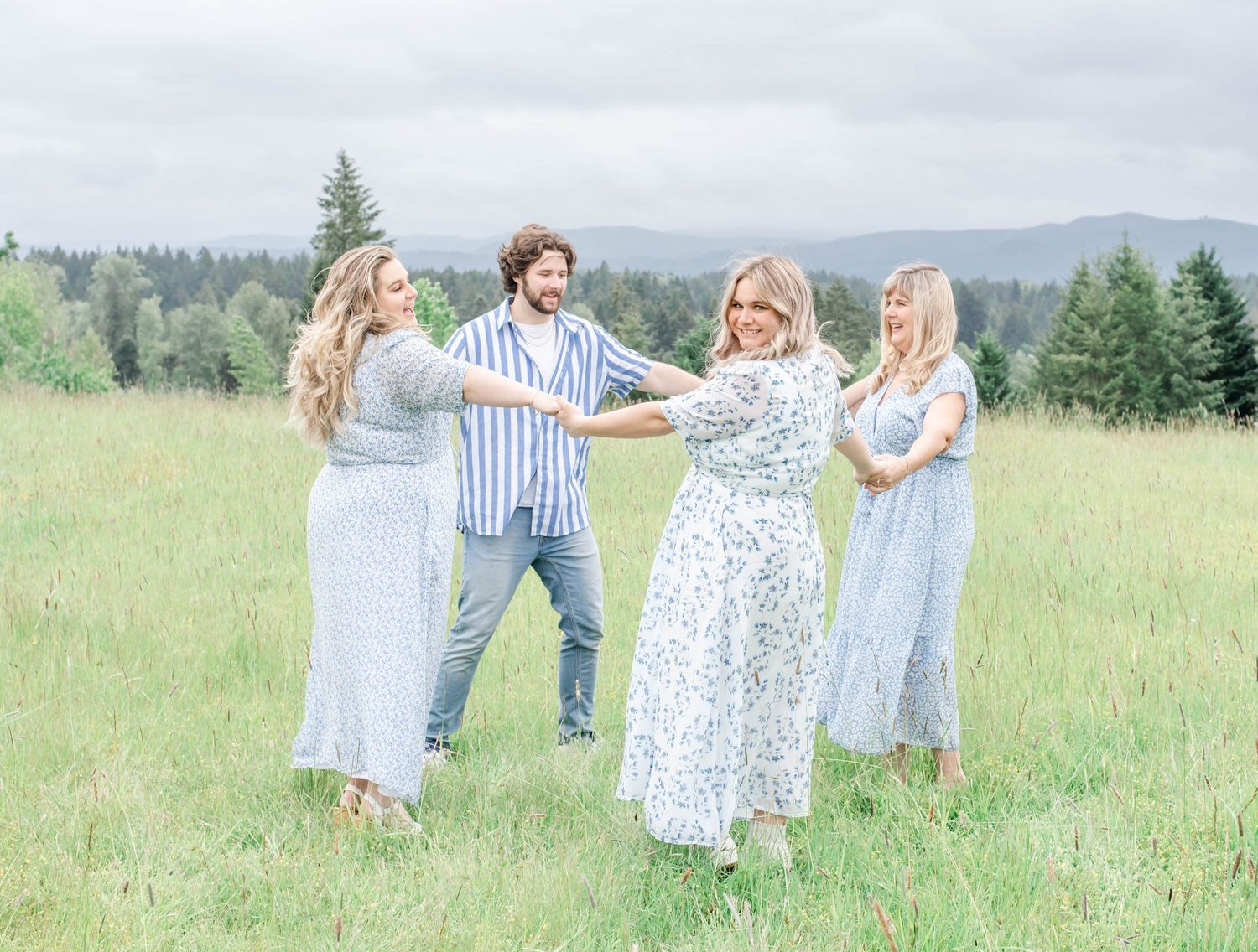 Group in coordinating blue dresses dance together in a mountain meadow.