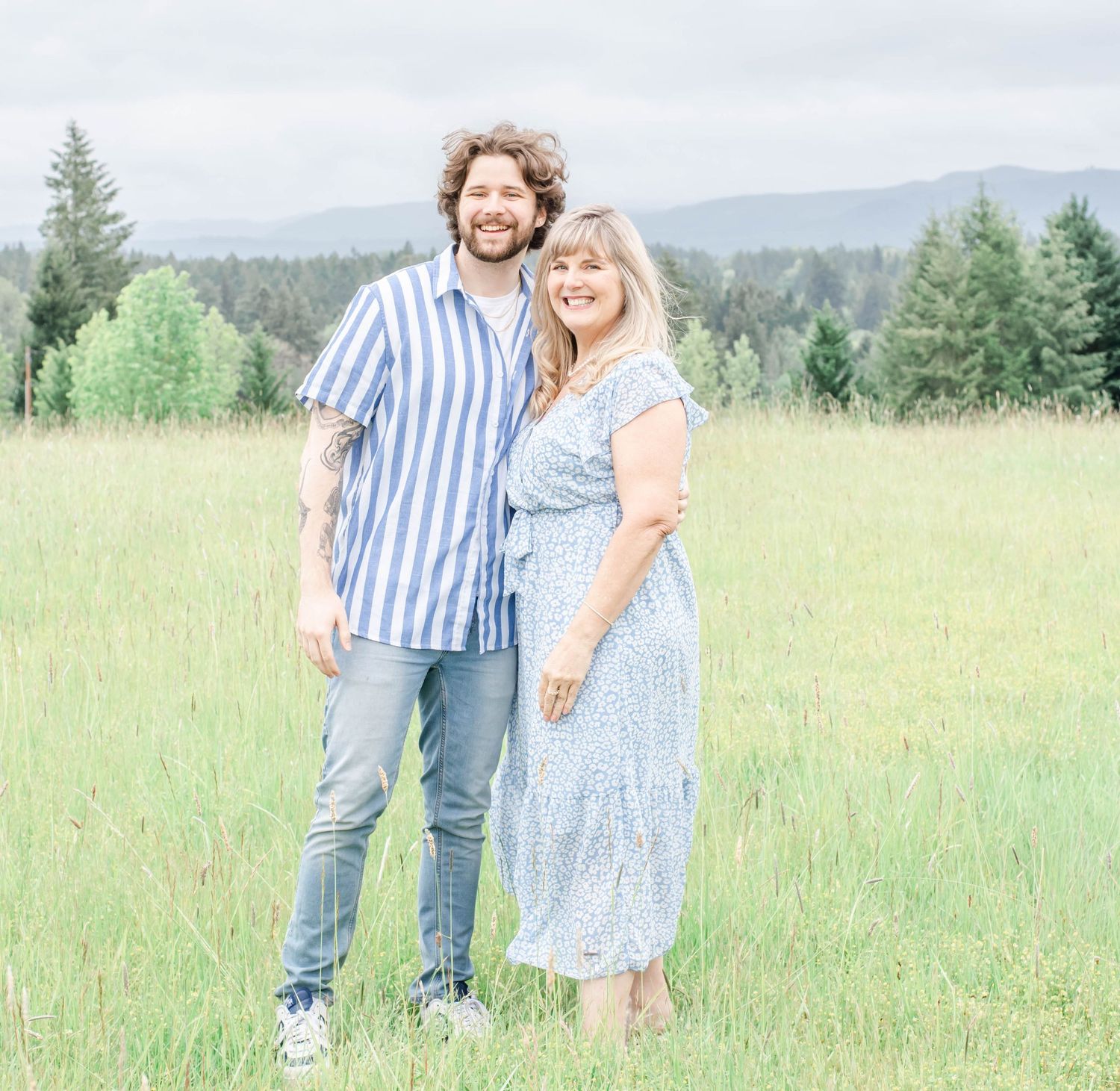 A couple poses together in blue stripes and floral dress against mountain scenery.