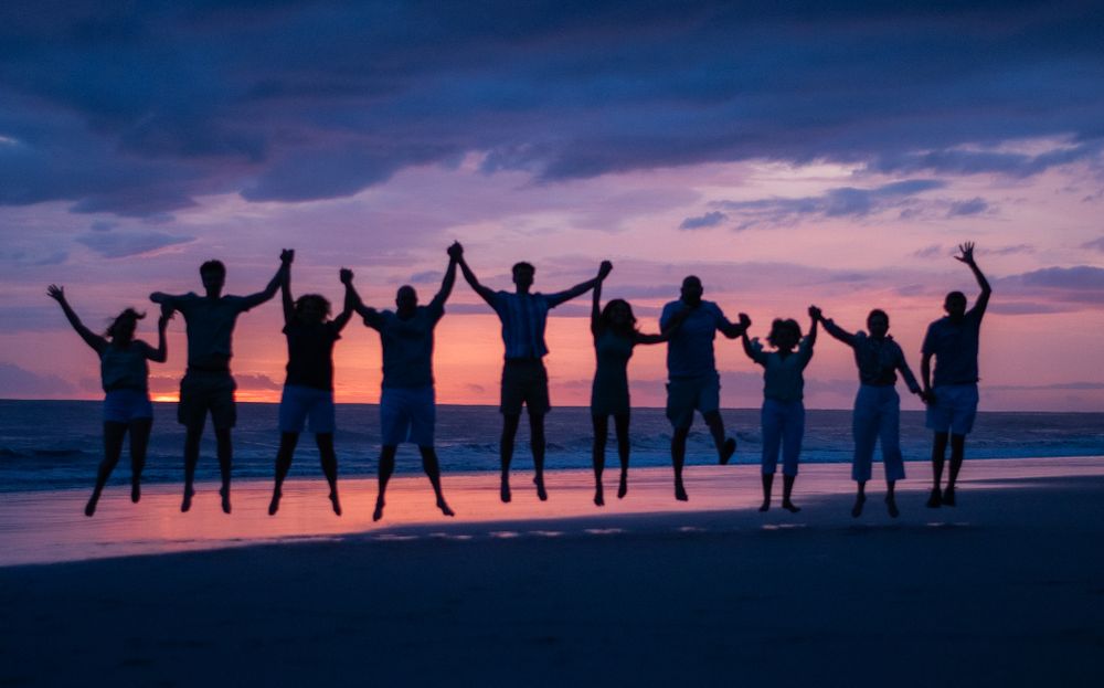 Silhouettes of people jumping with raised arms on a beach against a dramatic purple sunset sky.