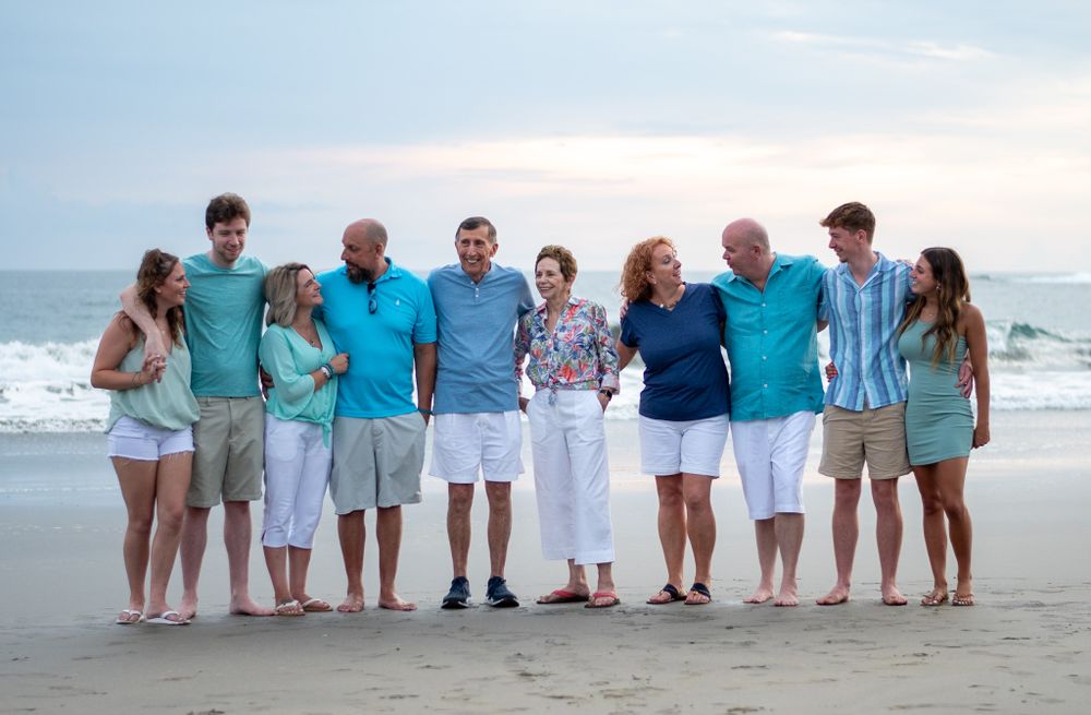 Family standing together on beach wearing coordinated blue and white outfits at sunset.