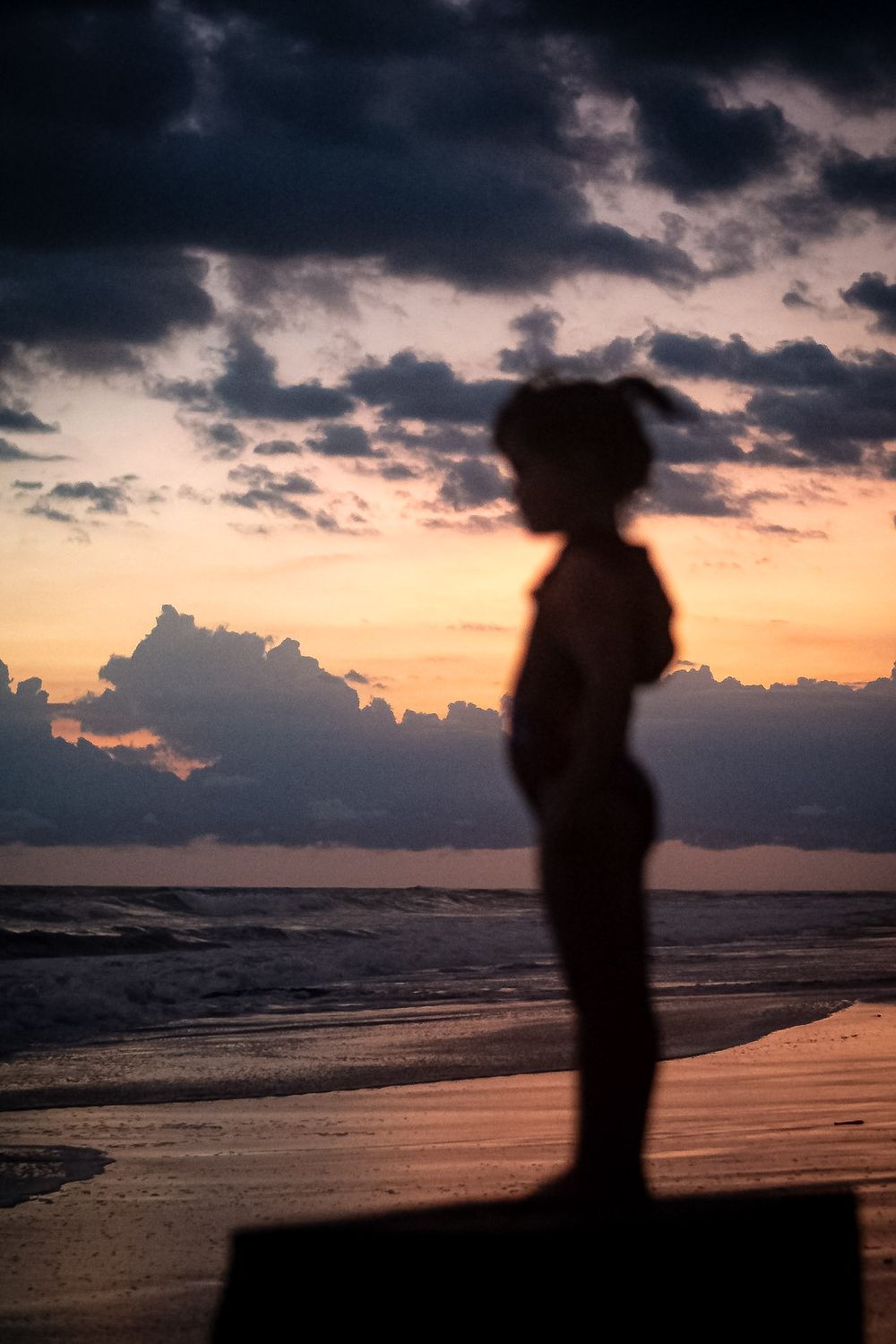 Silhouette of person standing on beach during colorful sunset with dramatic clouds.
