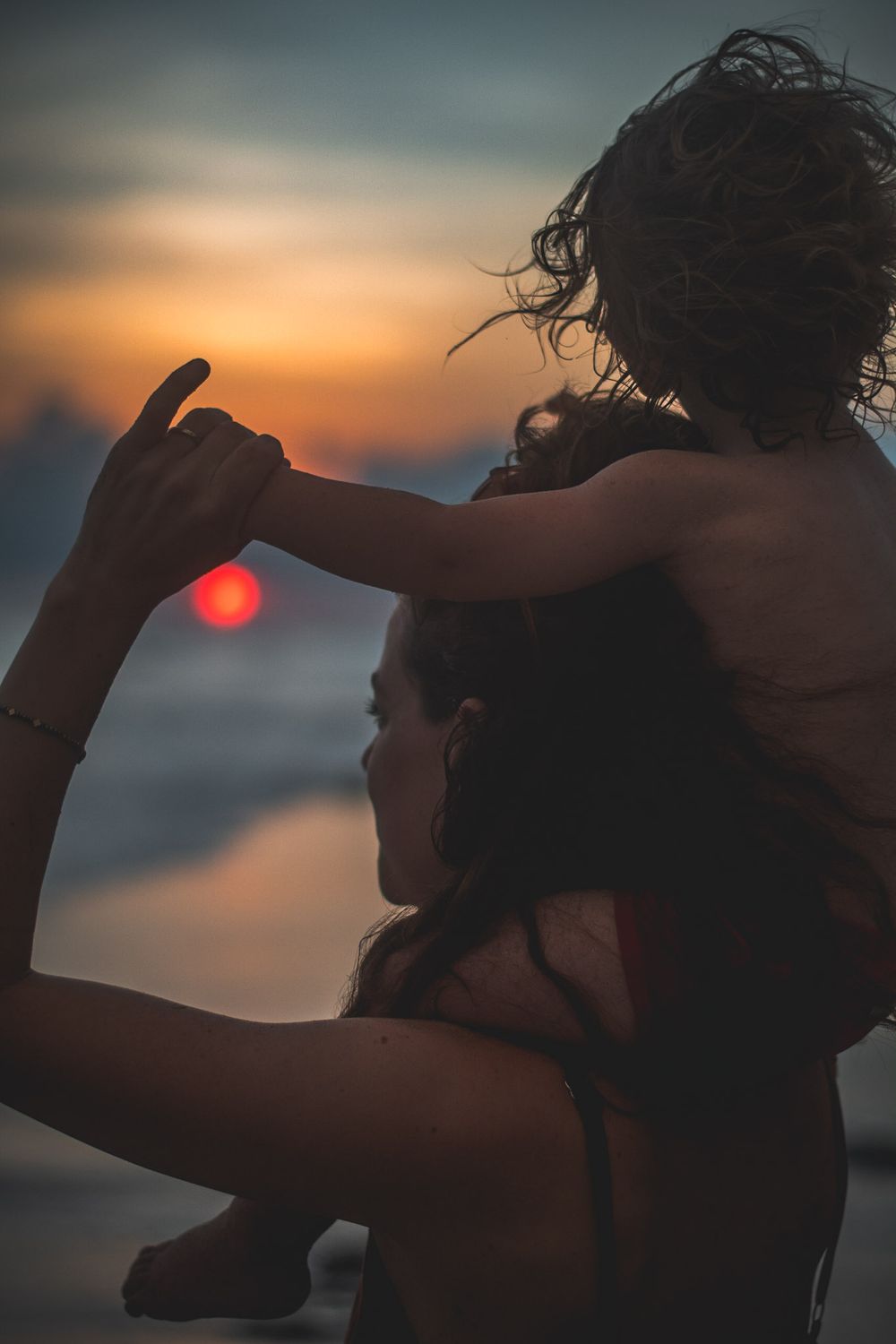 Silhouetted figures on beach at sunset with sun creating golden glow over ocean.