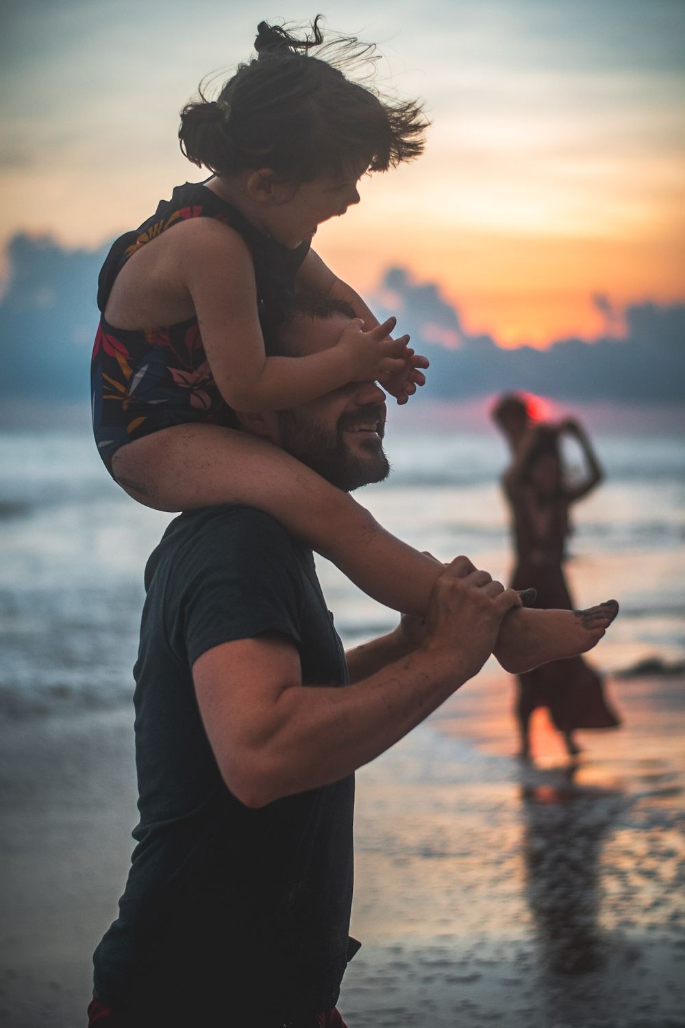 Silhouette of parent and child playing on beach at sunset with waves in background.