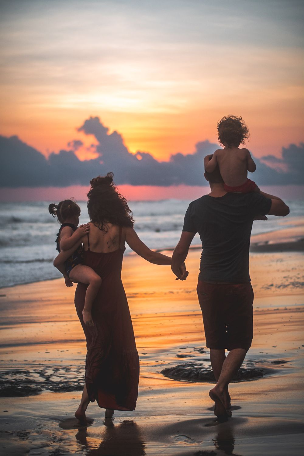 Silhouetted family walking together on beach at sunset holding hands.
