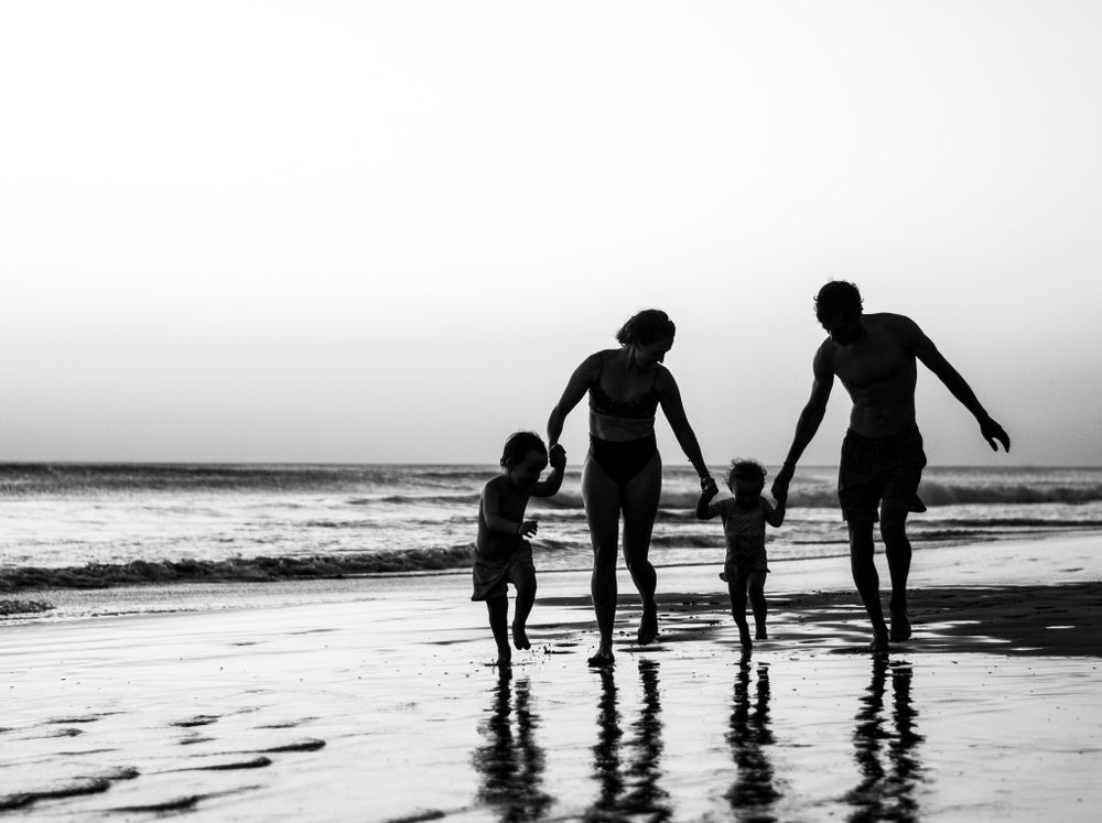 Silhouette of family holding hands while jumping on beach at sunset.