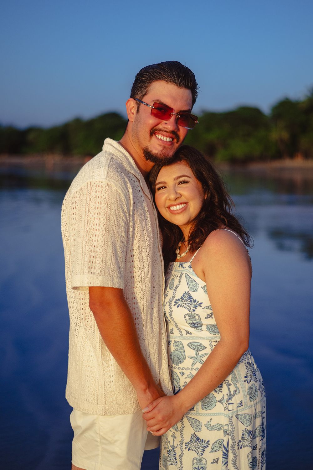 A happy couple in white beach attire poses together during golden hour.