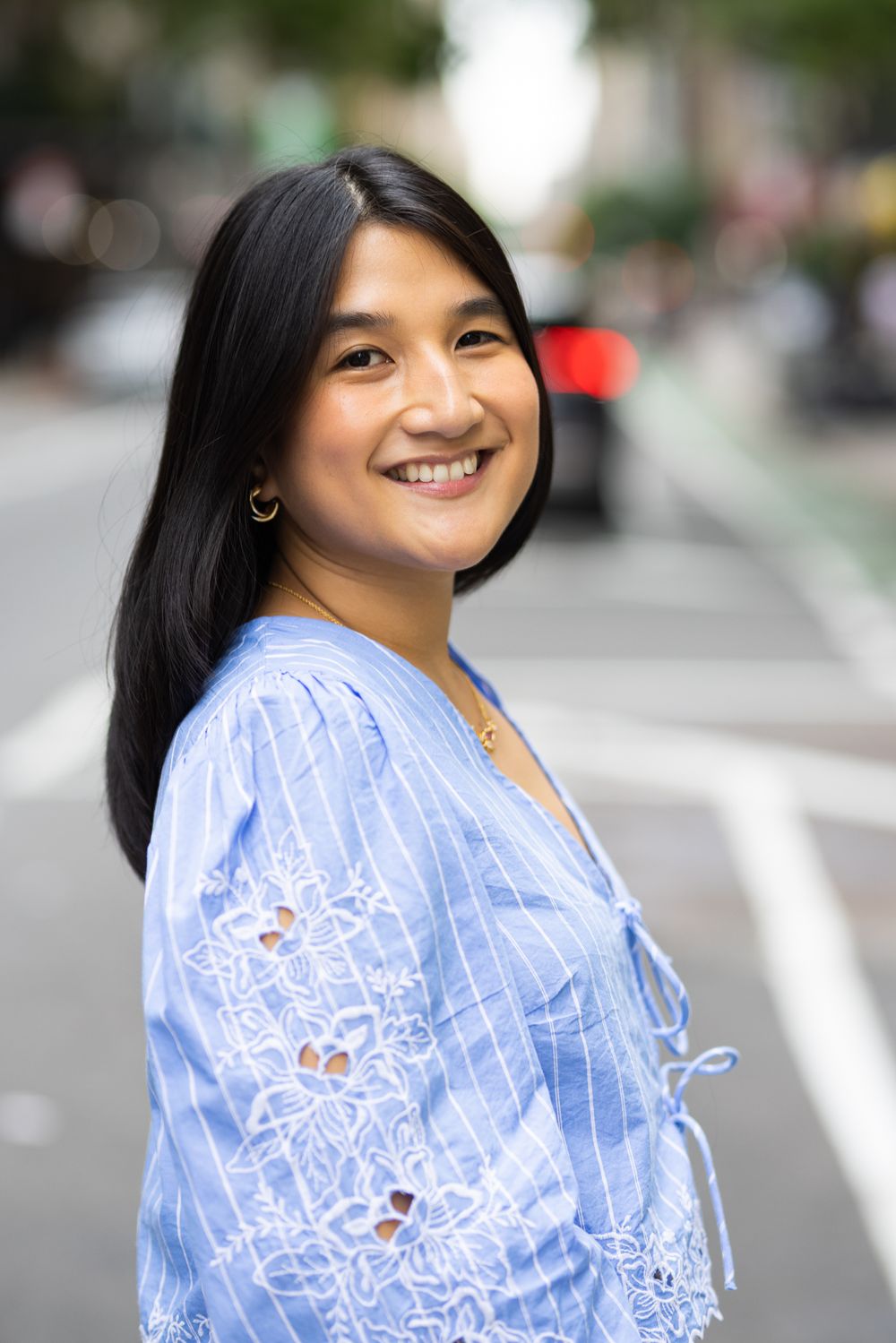 Smiling young Asian woman in blue floral blouse standing on urban city street.
