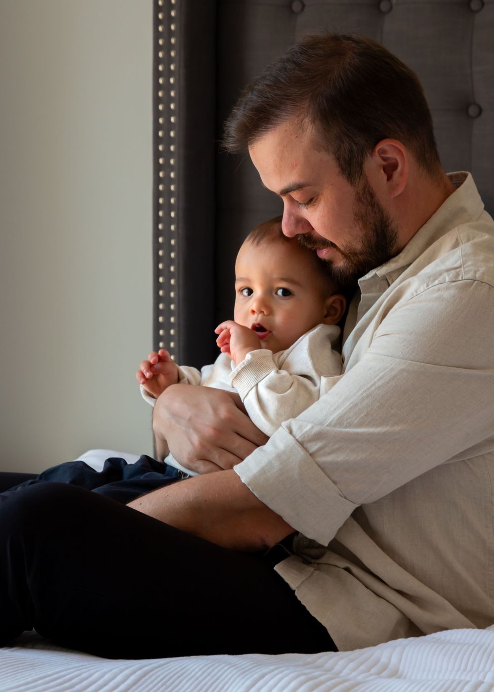 Baby sat on fathers lap on master bed at-home in dubai in quiet moment during at-home lifestyle family photoshoot