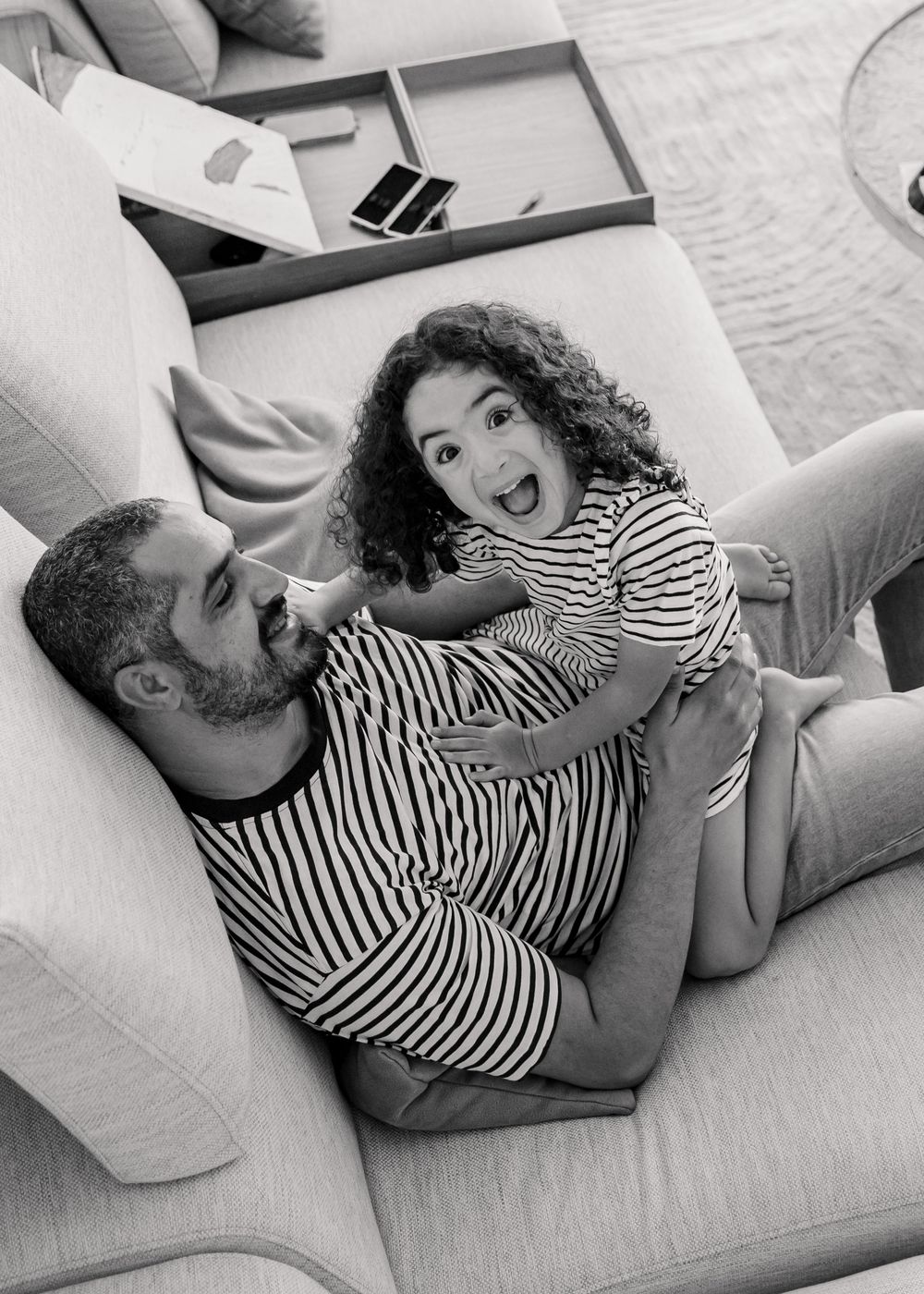 candid Black and white shot of father and young daughter sitting and laughing on the sofa at home during family maternity session in dabai