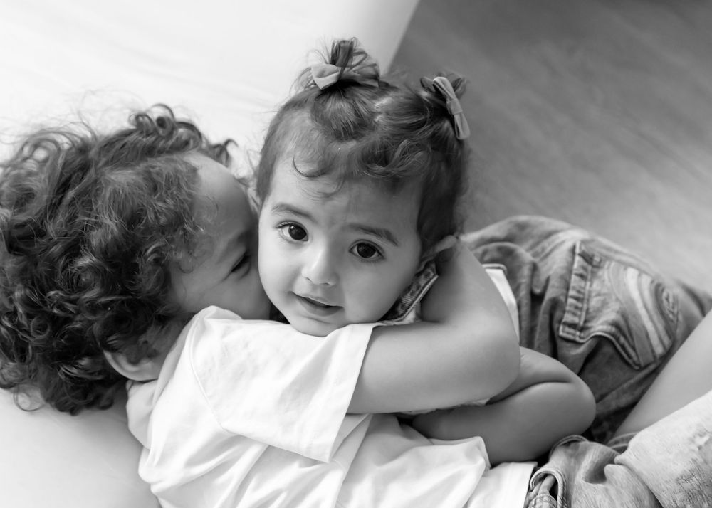 Brother and sister embrace on the floor whilst enjoying their at-home family photography session in Dubai. Black and white copy of original
