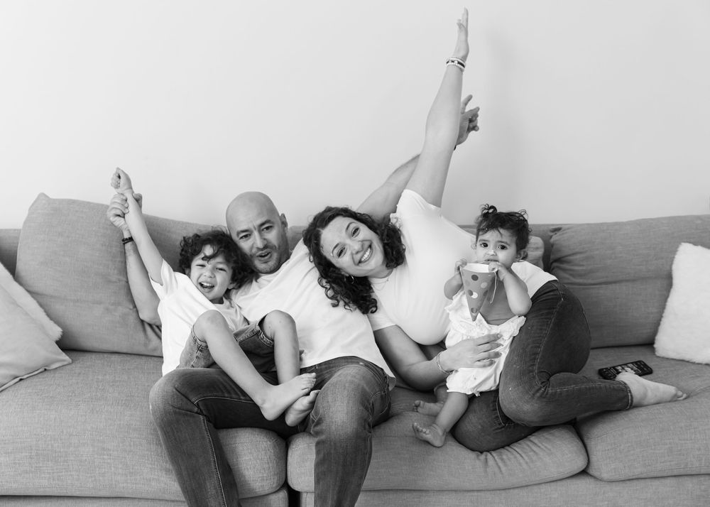 Black and white portrait of a family looking very happy on their sofa at home in Dubai during a family photoshoot with Carlene Thurston