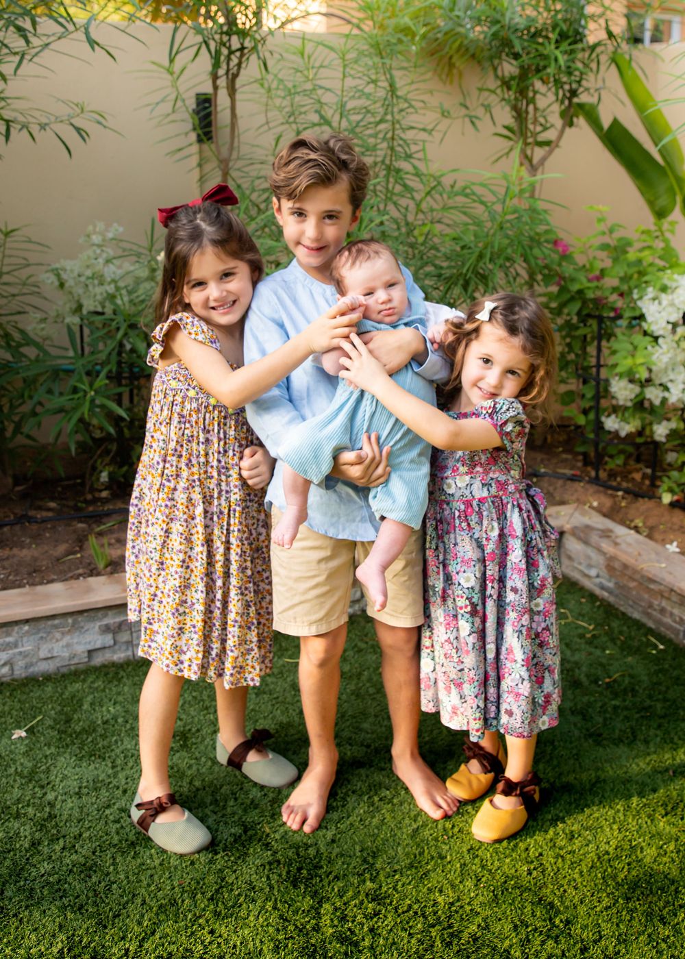 4 siblings including newborn baby posing for a portrait in their garden in Dubai during natural lifestyle family photoshoot