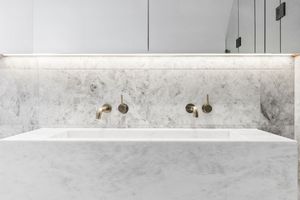 Modern bathroom sink carved from white marble with wall-mounted brass faucets and minimalist design.