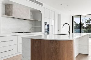 Modern white kitchen with wooden accents features sleek cabinetry, waterfall island, and floor-to-ceiling windows.