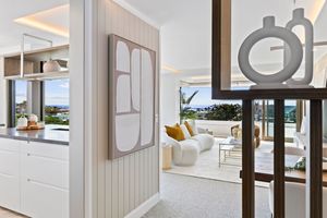 Modern white kitchen with sleek cabinets, pendant lights, and a large island featuring integrated appliances and bar seating.