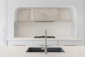 Modern white kitchen with sleek cabinets, black sink, and arched recessed shelving in the backsplash area.
