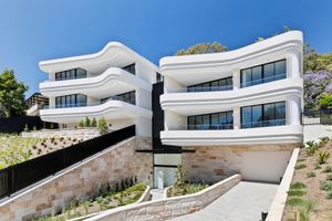 Modern white hillside villa with curved architecture and stone retaining walls overlooking a coastal landscape.