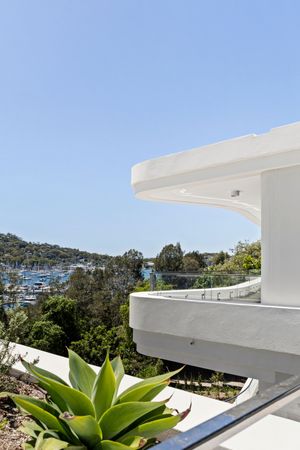 Modern white rooftop terrace with curved architectural details and succulent plants overlooking a marina and hillside.