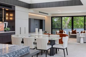 Modern office meeting room features white tables, gray chairs, and large windows overlooking lush greenery.