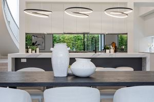 Modern dining area with white ceramic vases on dark wood table under circular pendant lights and large windows.