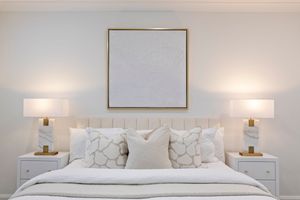 A modern white bedroom with upholstered headboard, bedside sconces, and neutral decor creates a serene atmosphere.
