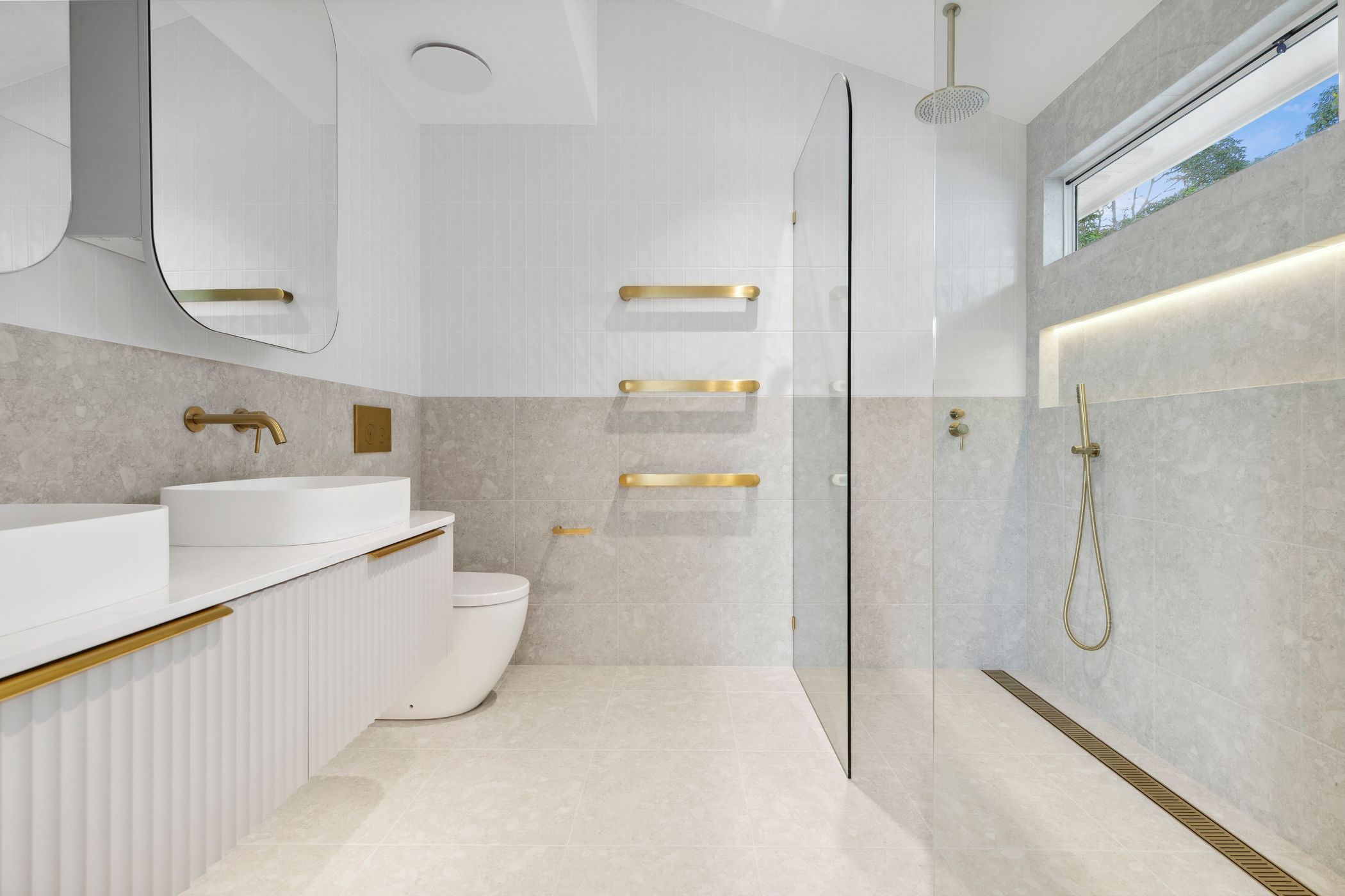 Modern white bathroom interior with gold accents featuring floating vanity, glass shower and textured wall tiles.