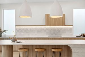 Modern white kitchen with curved wooden island bar, concrete backsplash, pendant lights and wooden bar stools.