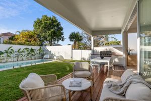 Modern outdoor patio with wicker furniture and cushions overlooking a manicured lawn and tropical landscaping.