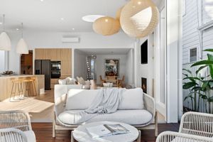 Modern open concept living room with white sofa, rattan chairs and pendant lights in a bright Scandinavian style interior.