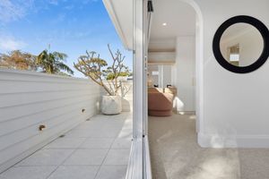 Modern white balcony with sliding glass doors opens to a bright interior room featuring a round mirror and tiled flooring.