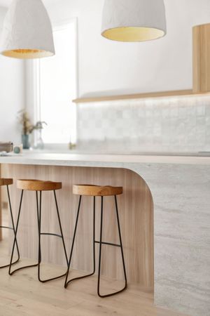 Modern kitchen counter with wooden bar stools and white pendant lights in a bright minimalist interior design.