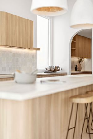 Modern kitchen interior with light wood cabinets, white countertops and minimalist pendant lights creating a bright space.