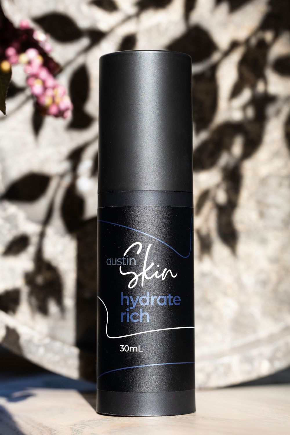 Black skincare product bottles with minimalist design against a blurred background with soft shadows and floral elements.
