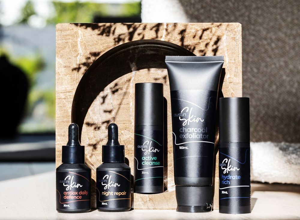 Black skincare product containers and tubes arranged in a row on a light surface with natural lighting.