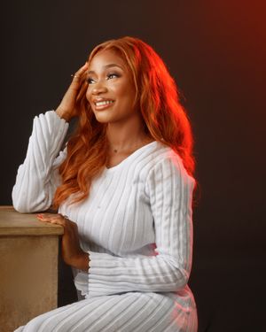 Woman in white sweater with copper hair poses against dark background with red lighting.
