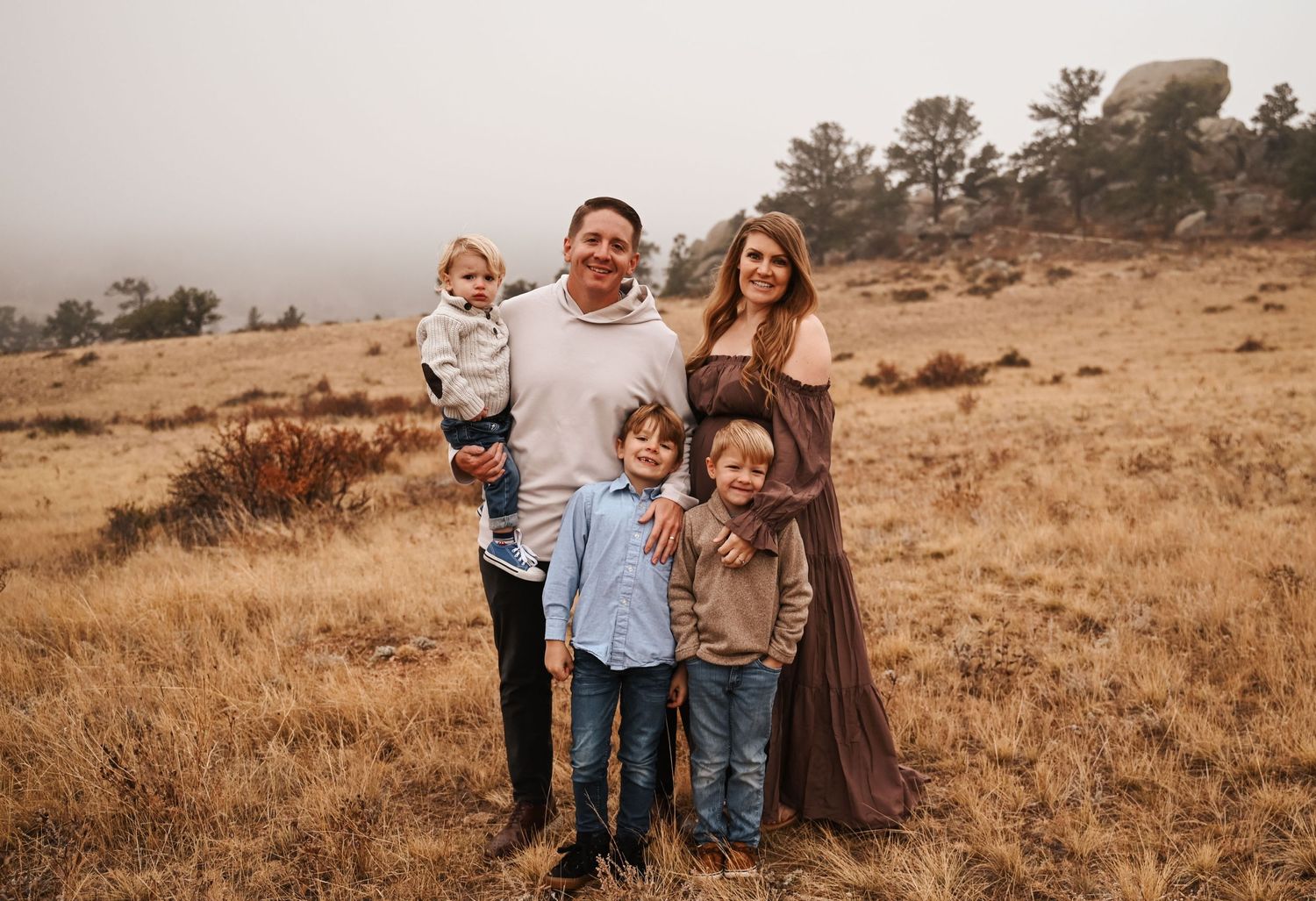 A family portrait session in a golden field with mountains in the background at sunset.