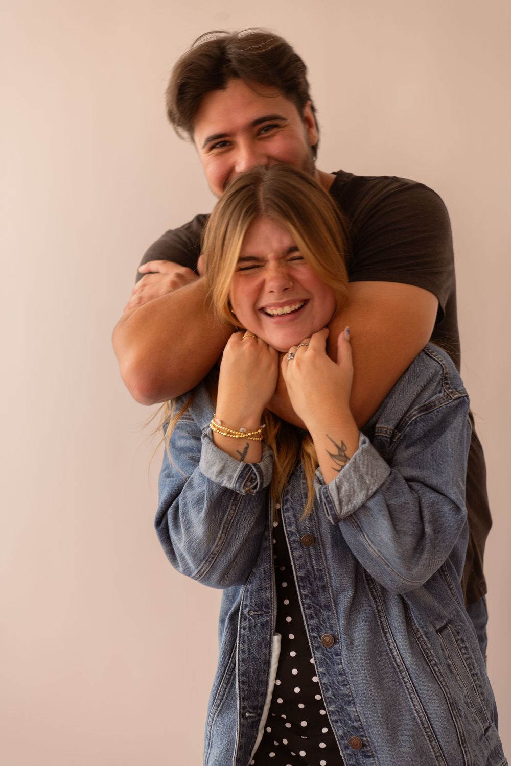 Man hugging laughing woman from behind, both wearing casual denim outfits.