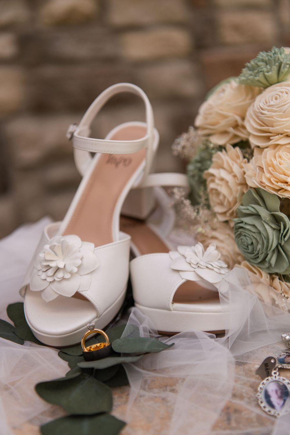 White bridal heels with flower detail beside wedding bouquet of roses and succulents.
