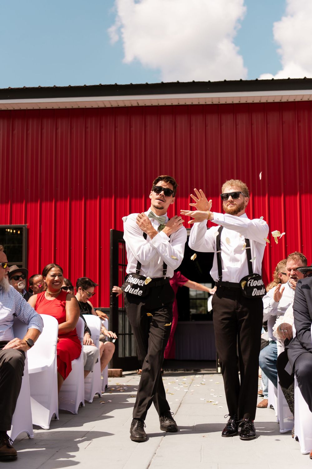Two groomsmen in suspenders and sunglasses performing fun entrance at outdoor wedding.