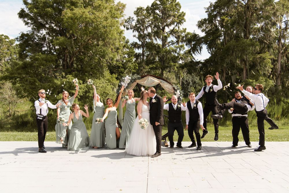 Wedding party celebrating with bride and groom under floral arch outdoors.