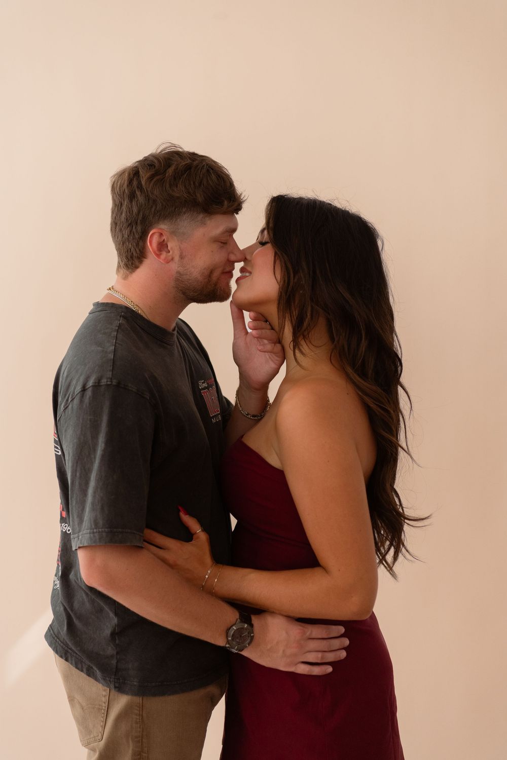 Couple in intimate moment, noses touching, woman in burgundy dress embraced by man in gray tee.