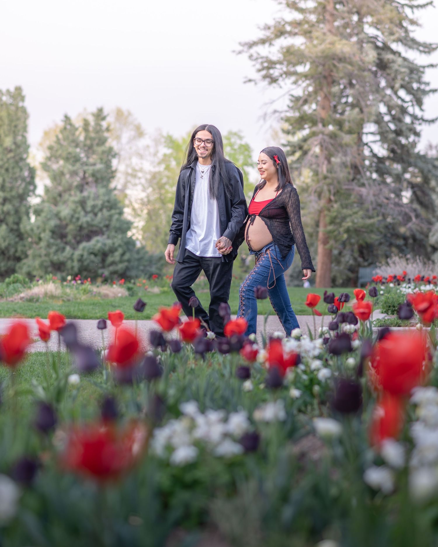 Couple walking through a vibrant garden filled with red, white and black  tulips. Downtown Denver maternity session.