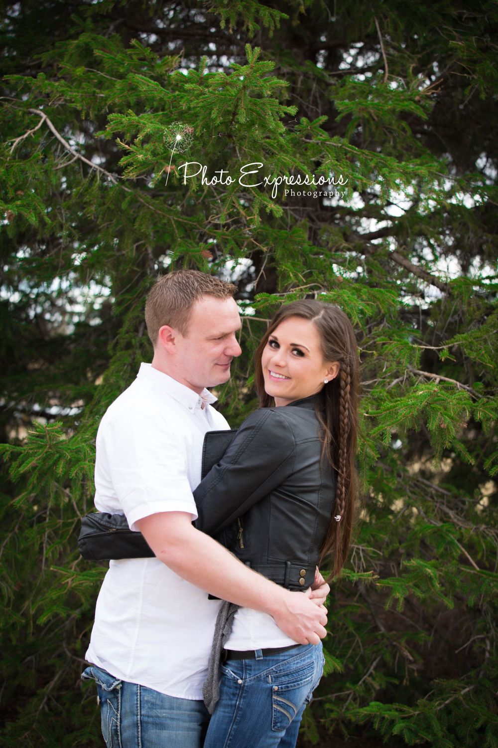Playful couple embracing by evergreen trees during outdoor photo session.