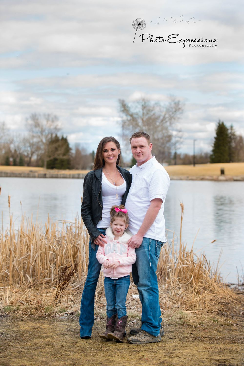 Family portrait session by a lake with tall grasses and natural scenery in the background.