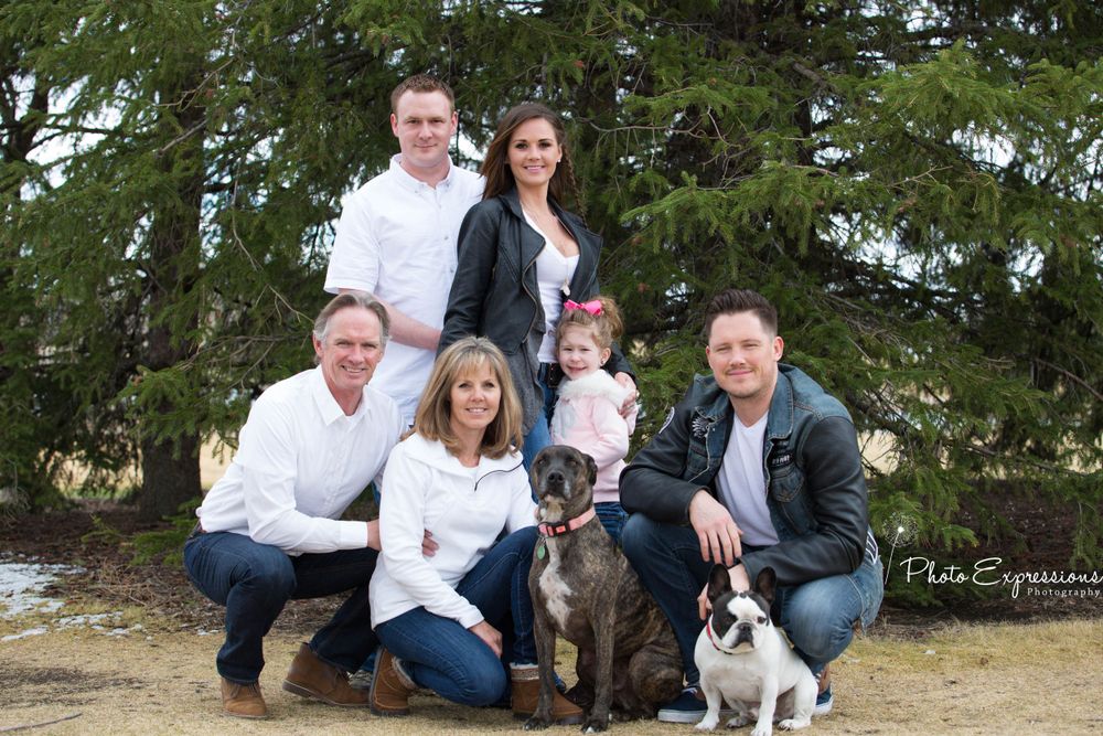 Family photo session outdoors including a black and white dog posing with the group.
