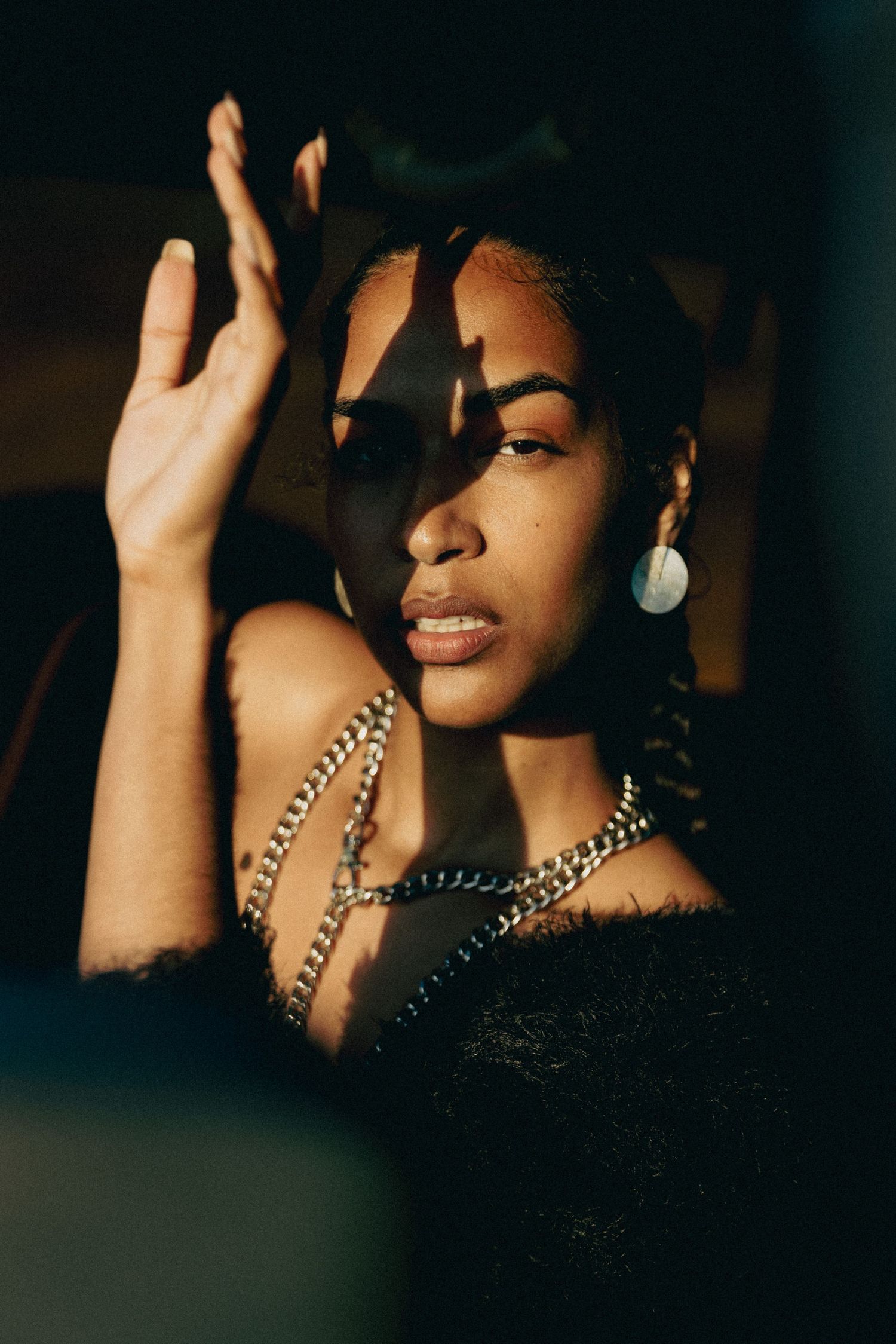 Artistic portrait with dramatic shadows and gold chain accessories.